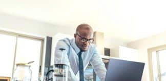 Geschäftsmann mit einem Laptop auf dem Küchentisch zu Hause. Mann arbeitet, während er frühstückt.